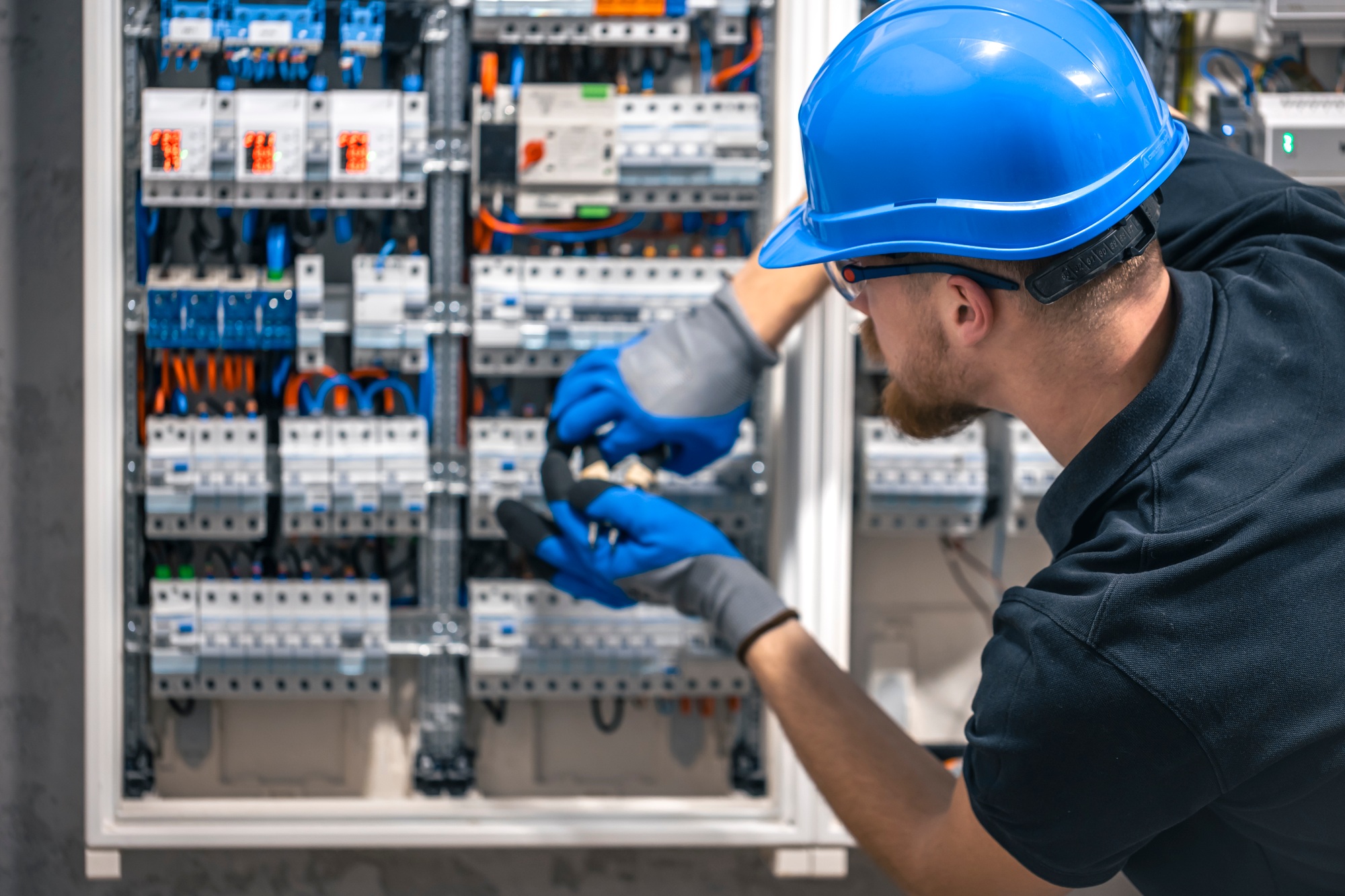 A male electrician works in a switchboard with an electrical connecting cable.